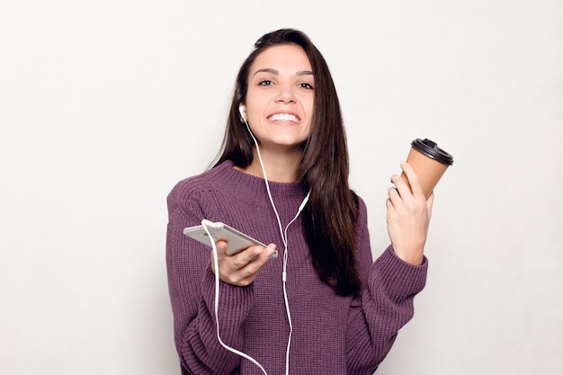 Technologie, mode de vie, dépendance à Internet et concept de personnes - Belle jeune femme avec un téléphone intelligent. Femme séduisante heureuse et souriante en regardant le téléphone portable. Mur gris à l'arrière-plan.