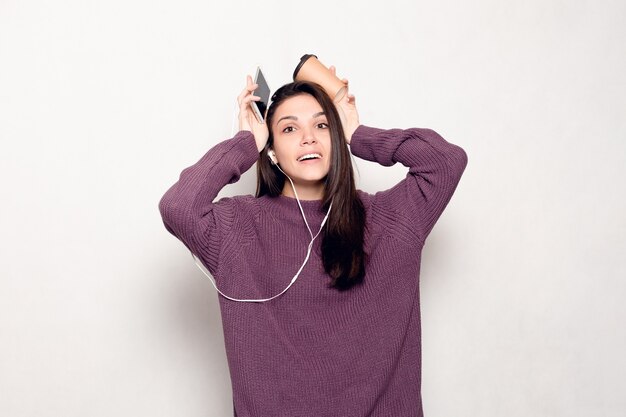 Technologie, mode de vie, dépendance à Internet et concept de personnes - Belle jeune femme avec un téléphone intelligent. Femme séduisante heureuse et souriante en regardant le téléphone portable. Mur gris à l'arrière-plan.