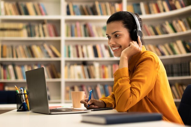 Technologie moderne et apprentissage en ligne heureuse femme métisse dans le casque regardant un webinaire en ligne assis dans