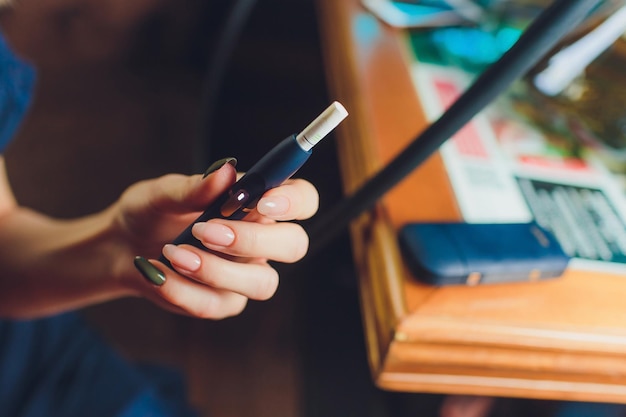 Photo technologie de produit du tabac non brûlé par la chaleur femme tenant une e-cigarette dans sa main avant de fumer