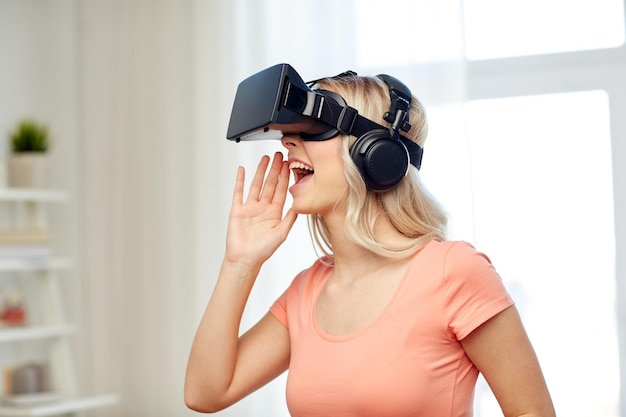 technologie, réalité virtuelle, divertissement et concept de personnes - jeune femme heureuse dans un casque de réalité virtuelle ou des lunettes et des écouteurs 3d jouant à la maison et appelant quelqu'un