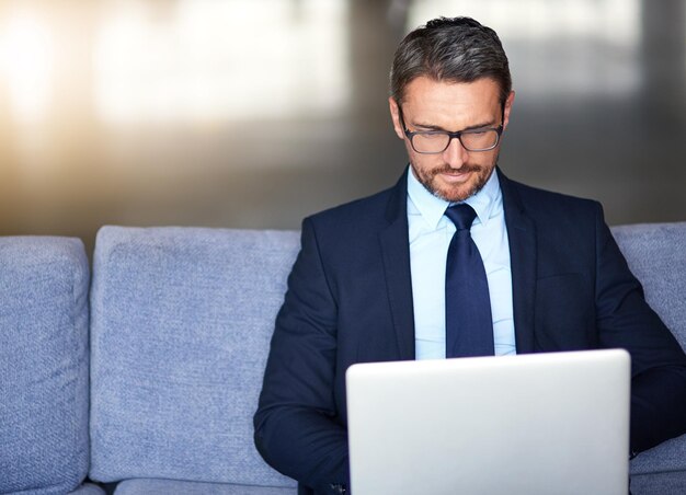 La technologie sans fil lui rapproche les opportunités d'affaires Photo d'un homme d'affaires utilisant un ordinateur portable sur le canapé