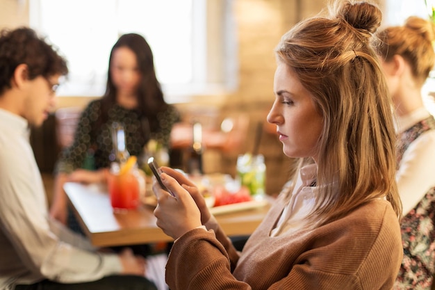 technologie, style de vie, vacances et concept de personnes - femme avec smartphone et amis au restaurant