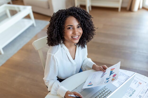 Technologie de travail à distance et concept de personnes heureuse souriante jeune femme d'affaires avec ordinateur portable et papiers travaillant au bureau à domicile pendant la crise sanitaire de Covid19