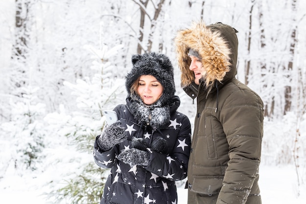 Technologies et concept de relation - Heureux couple souriant prenant un selfie dans une forêt d'hiver à l'extérieur.