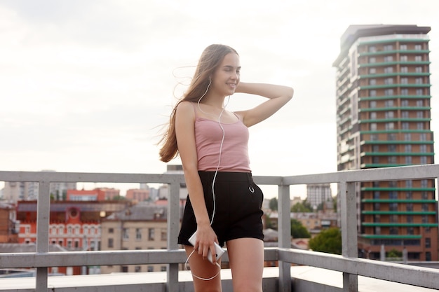 Technologies, émotions, personnes, musique, beauté, mode et concept de style de vie - Jeune femme avec des écouteurs suspendus à son téléphone portable alors qu'elle marche dans une rue urbaine, vue d'une hauteur