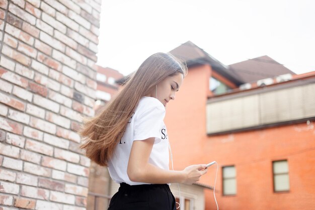 Technologies, émotions, personnes, musique, beauté, mode et concept de style de vie - Jeune femme avec des écouteurs suspendus à son téléphone portable alors qu'elle marche dans une rue urbaine, vue d'une hauteur