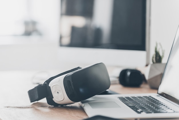 Technologies modernes. Gros plan sur un casque VR posé sur le bureau et près d'un ordinateur portable et d'un ordinateur