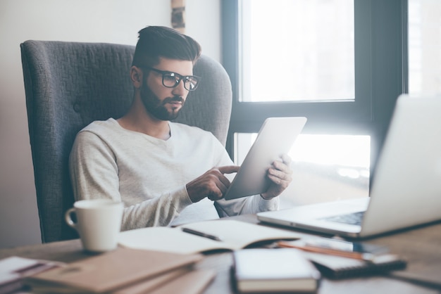 Des technologies qui facilitent la vie. Jeune homme confiant à lunettes travaillant sur tablette numérique alors qu'il était assis au bureau ou au café