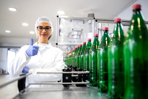 Technologue féminine montrant les pouces vers le haut et représentant une production de boissons réussie en usine