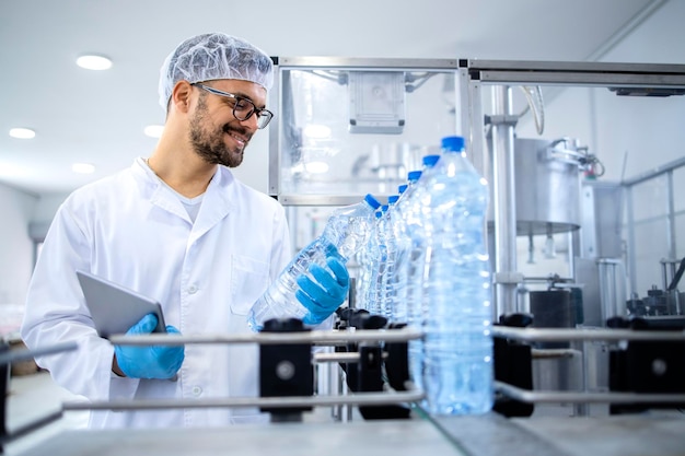 Technologue industriel vérifiant la production d'eau en bouteille dans l'usine d'embouteillage sur la machine