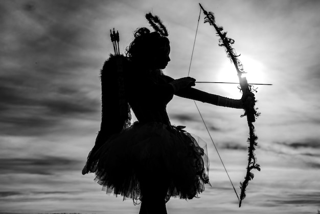 Photo teen angel girl archer au coucher du soleil silhouette d'un cupidon mignon teen cupidon sur le fond de ciel nuage v