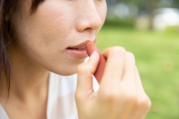 Teen asiatique avec rouge à lèvres à l'extérieur pour la protection UV gros plan sur ses lèvres