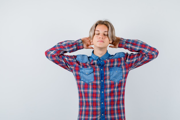 Teen boy en chemise à carreaux avec les mains derrière la tête et l'air détendu , vue de face.