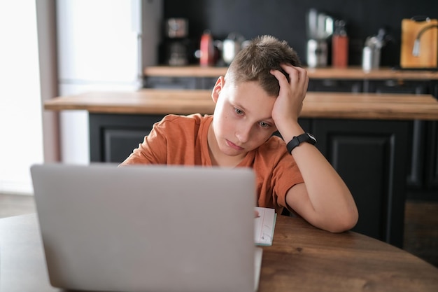 Teen boy étudie ou joue à un jeu sur fond intérieur de maison d'ordinateur portable