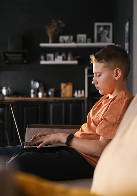 Teen boy étudie ou joue à un jeu sur fond intérieur de maison d'ordinateur portable