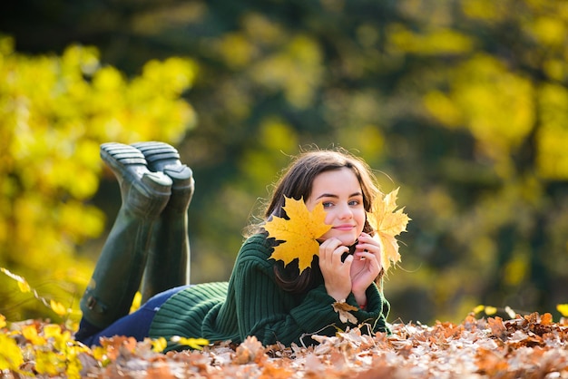 Teen dans le parc en automne. Souriante jeune fille allongée sur les feuilles d'érable d'automne à l'automne à l'extérieur. Portrait d'une belle adolescente souriante. Jeune adolescente à la recherche d'appareil photo.