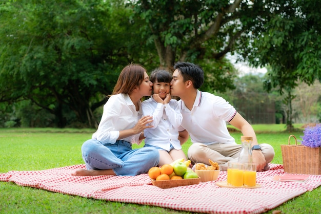 Teen famille asiatique moment de pique-nique de vacances heureux dans le parc avec le père, la mère embrassant la fille et le sourire pour passer des vacances