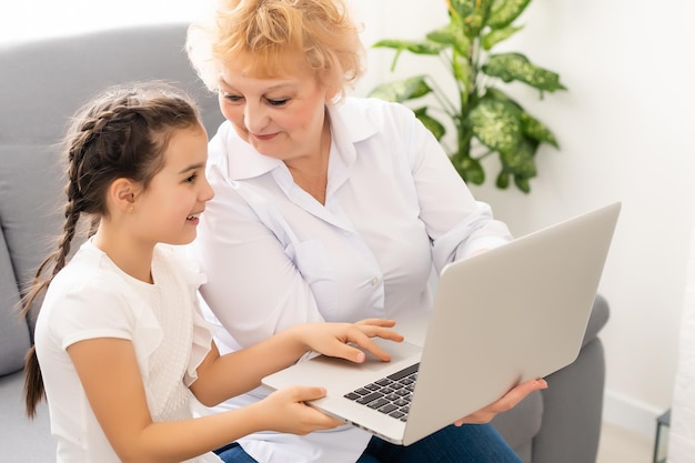 Teen girl apprentissage à distance cours en ligne virtuel à distance sur appel vidéo leçon virtuelle avec grand-mère, étudiant à la maison à l'aide d'un ordinateur portable. grand-parent ou tuteur aidant sa fille à distance