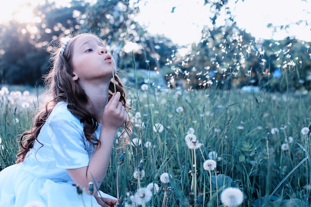 Teen girl blowing seeds d'une fleur de pissenlit dans un parc de printemps