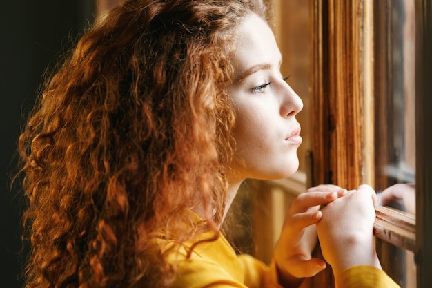 Teen girl curly gingembre dans la chemise jaune à la recherche de la grande fenêtre à l'intérieur du loft