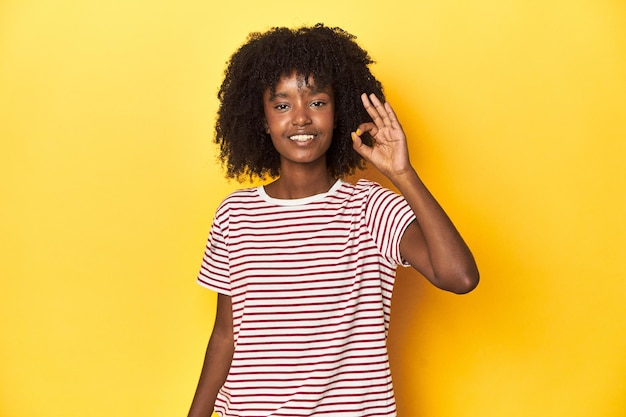 Teen girl in red striped Tshirt jaune studio toile de fond joyeuse et confiante montrant un geste correct