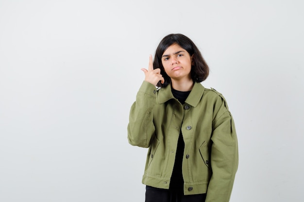 Teen girl pointant vers le haut dans la veste verte de l'armée et à la triste , vue de face.