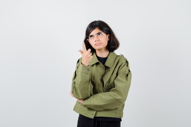 Teen girl pointant vers le haut en t-shirt, veste et à la réflexion. vue de face.