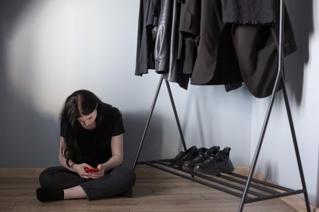 Teen girl with red smartphone en jean noir et un t-shirt près du cintre avec des vêtements noirs