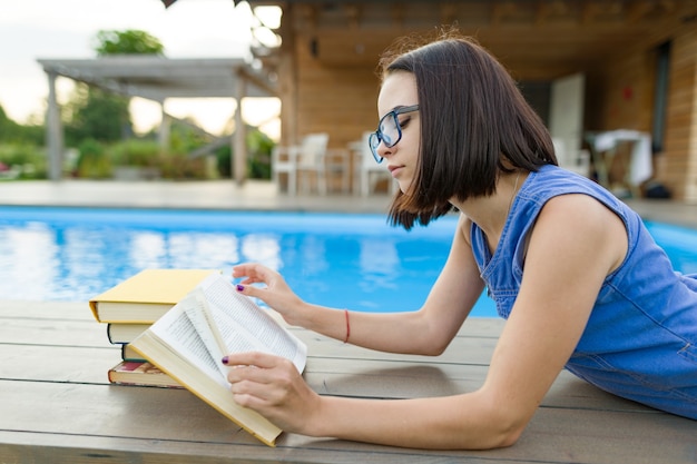 Teen woman reading book dans un espace privé près de la maison et de la piscine