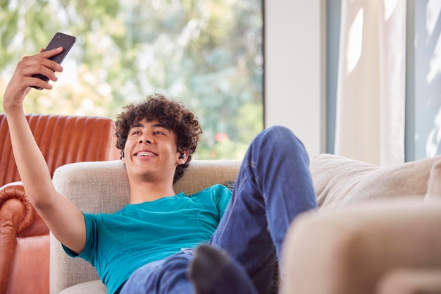 Teenage Boy Lying On Sofa At Home Prendre Selfie pour les médias sociaux sur téléphone mobile