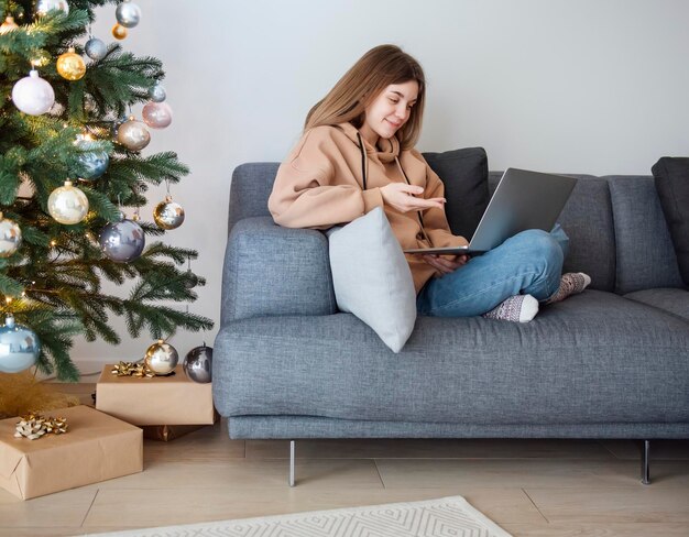 Teenage girl with laptop sitting on sofa in living room près de l'arbre de Noël