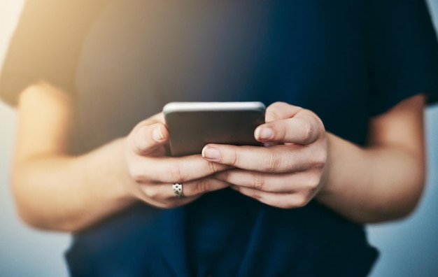 Téléchargement d'une nouvelle application Prise de vue en studio d'une jeune femme méconnaissable utilisant son téléphone portable sur un fond gris