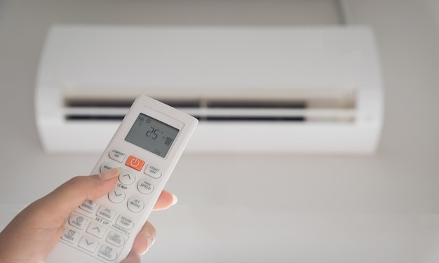 Télécommande tenant la main dirigée sur le climatiseur à l'intérieur de la pièce et réglée à température ambiante, 25 degrés Celsius.