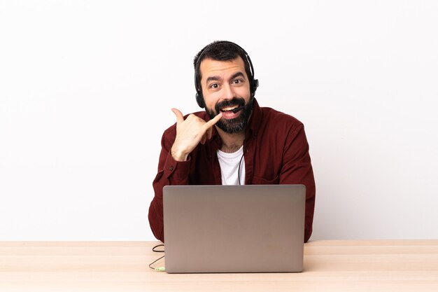 Telemarketer homme caucasien travaillant avec un casque et avec un ordinateur portable faisant le geste du téléphone