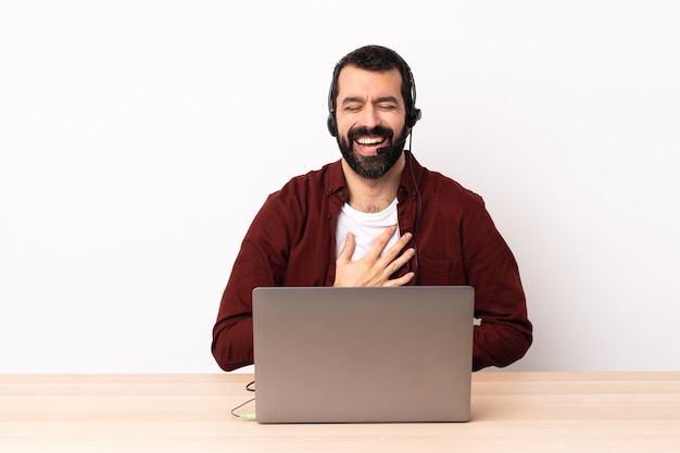 Telemarketer homme caucasien travaillant avec un casque et avec un ordinateur portable souriant beaucoup