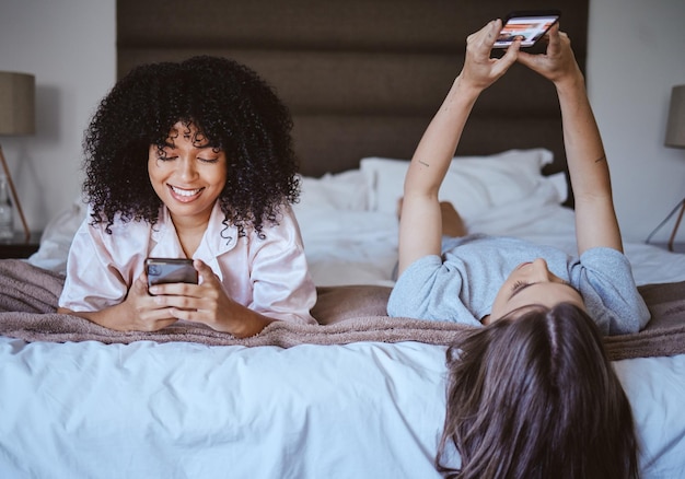 Téléphone d'appel vidéo et amis avec des femmes à la soirée pyjama pour la communication Internet et le contact Heureux se détendre et sourire avec une fille allongée dans la chambre avec la technologie numérique et les médias sociaux ensemble