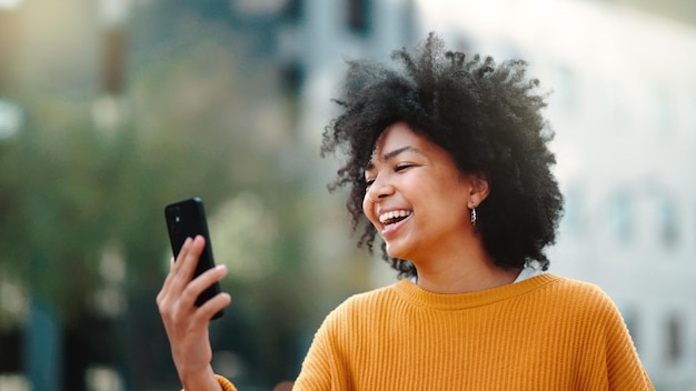 Téléphone d'appel vidéo et femme noire dans la ville parlant de mise à jour de voyage en ligne et de communication 5g ou de chat drôle Rire personne ou étudiant de la génération z sur téléphone portable mobile et diffusion en direct pour l'extérieur urbain