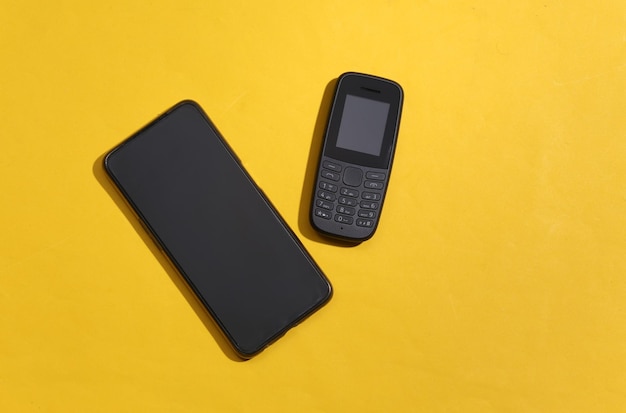 Téléphone à bouton-poussoir et smartphone moderne sur fond jaune. Vue de dessus