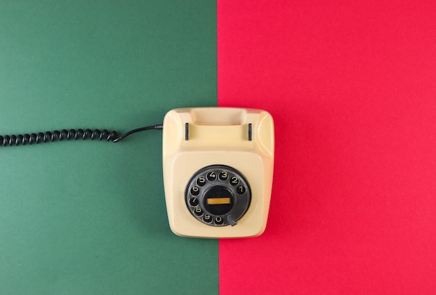 Téléphone à cadran rétro sur une surface de papier rouge-vert.