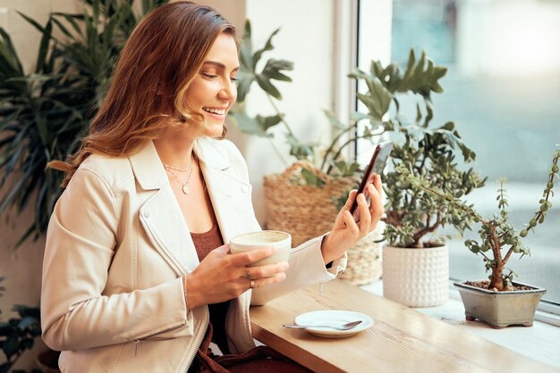 Téléphone de café et médias sociaux avec une cliente buvant tout en tapant un message texte par une fenêtre Internet café mobile et communication avec une femme prenant un verre dans un restaurant