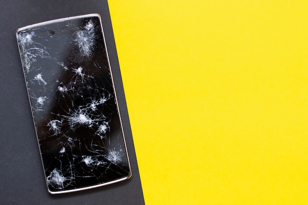 Un téléphone cassé sur fond jaune et noir. Appareil écrasé avec écran cassé représentant un accident. Écran texturé avec dommages. Verre foncé d'un écran.