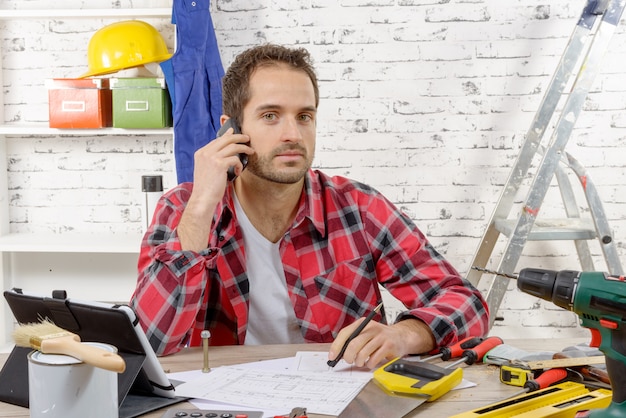 Téléphone de charpentier souriant assis sur le bureau, dans son atelier