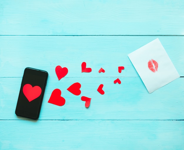 Téléphone avec un coeur rouge sur l'écran qui sur fond bleu avec coeurs et rose rouge