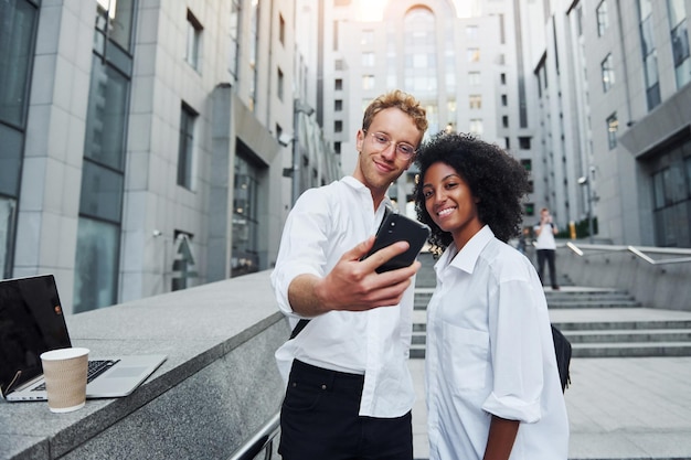 Avec le téléphone dans les mains Homme avec une femme afro-américaine ensemble dans la ville à l'extérieur