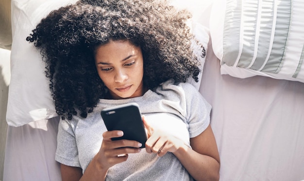 Téléphone femme noire et vue de dessus dans la chambre à coucher pour envoyer des SMS sur les réseaux sociaux ou naviguer sur Internet le matin Technologie lit relax et femme avec smartphone mobile pour le défilement Web ou la mise en réseau