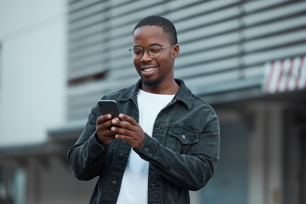 Photo téléphone d'homme noir et médias sociaux dans la ville lisant un message texte ou une communication sur l'application de réseau social conversation de chat d'une personne afro-américaine et heureux sur un smartphone mobile 5g à atlanta sourire