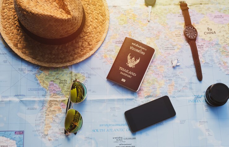 Téléphone intelligent, clé, objectif, avion, chapeau de paille et passeport sur carte avec effet de lumière solaire