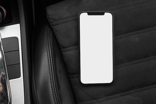 Téléphone intelligent avec écran blanc vierge sur siège auto en cuir dans le véhicule