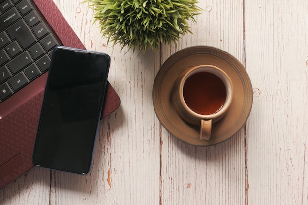 Téléphone intelligent avec écran vide, ordinateur portable sur table en bois.